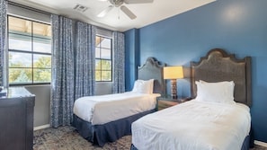 Une chambre d’hôtel avec deux lits, un ventilateur de plafond, une fenêtre avec des rideaux et une table de chevet avec une lampe.