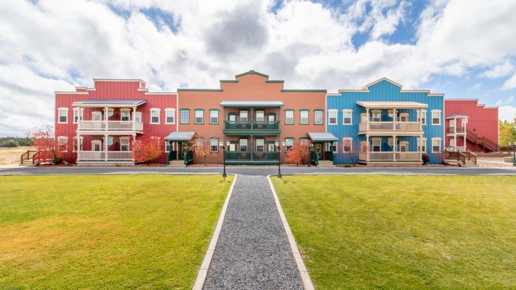 A row of colorful townhouses with a central entrance, a gravel pathway, and a grassy lawn.