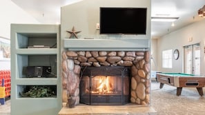 A fireplace with a stone surround, a television mounted above it, and a pool table in the background.