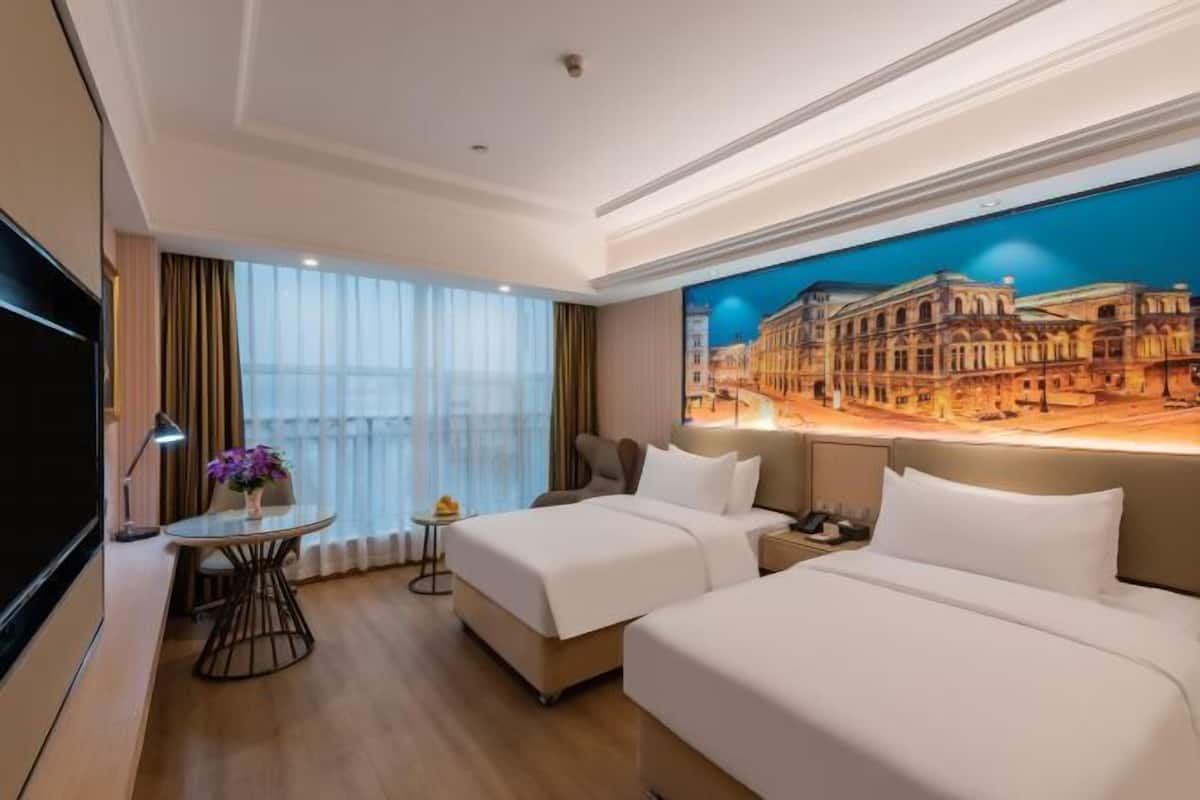 A hotel room with two beds, a desk, a chair, a TV, and a large window.