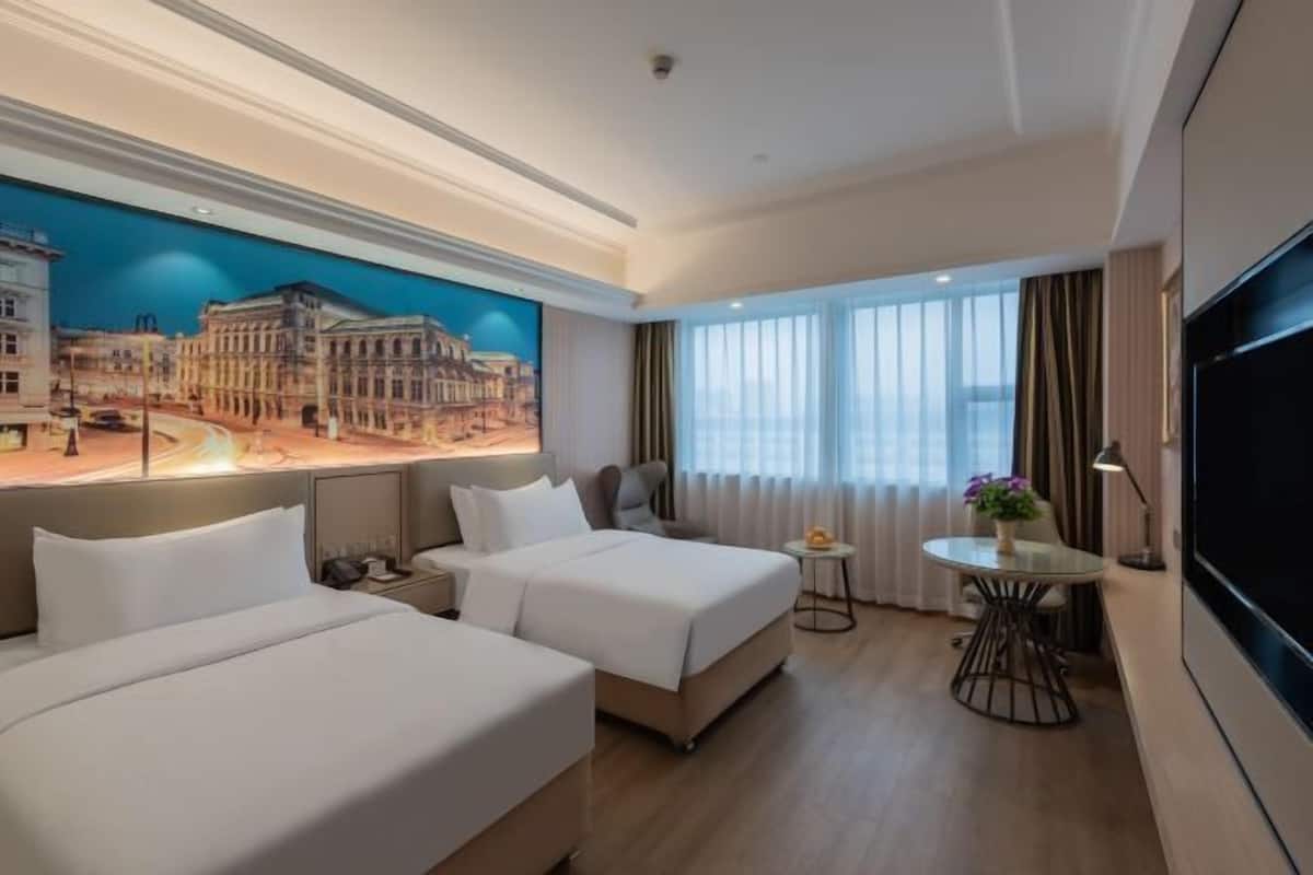 A hotel room with two beds, a TV, a small table with a plant, and a cityscape mural on the wall.