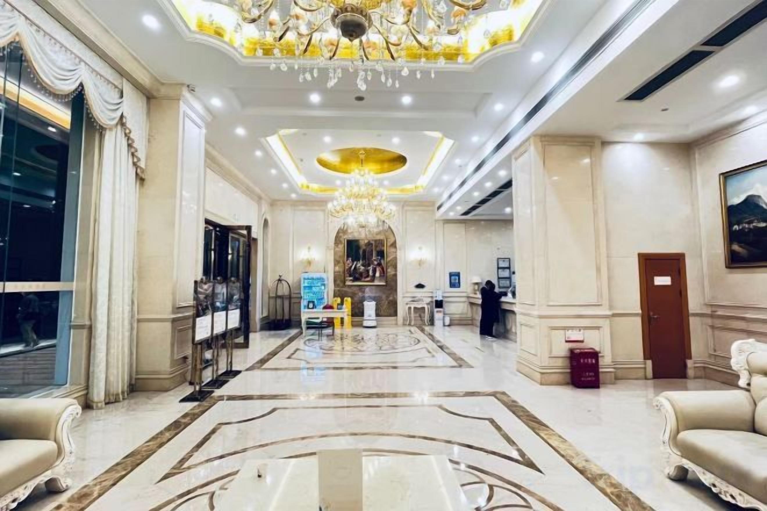 A hotel lobby with a grand chandelier, a reception desk, and a marble floor.