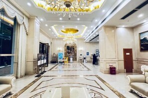 A hotel lobby with a grand chandelier, a reception desk, and a marble floor.