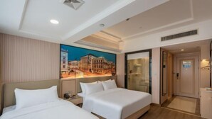 A hotel room with two beds, a large painting on the wall, a built-in desk, and a separate bathroom.