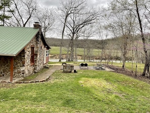 Une cabane en pierre avec un toit végétalisé, un espace de pique-nique équipé de bancs et d’une table, et une vue sur un lac entouré d’arbres.