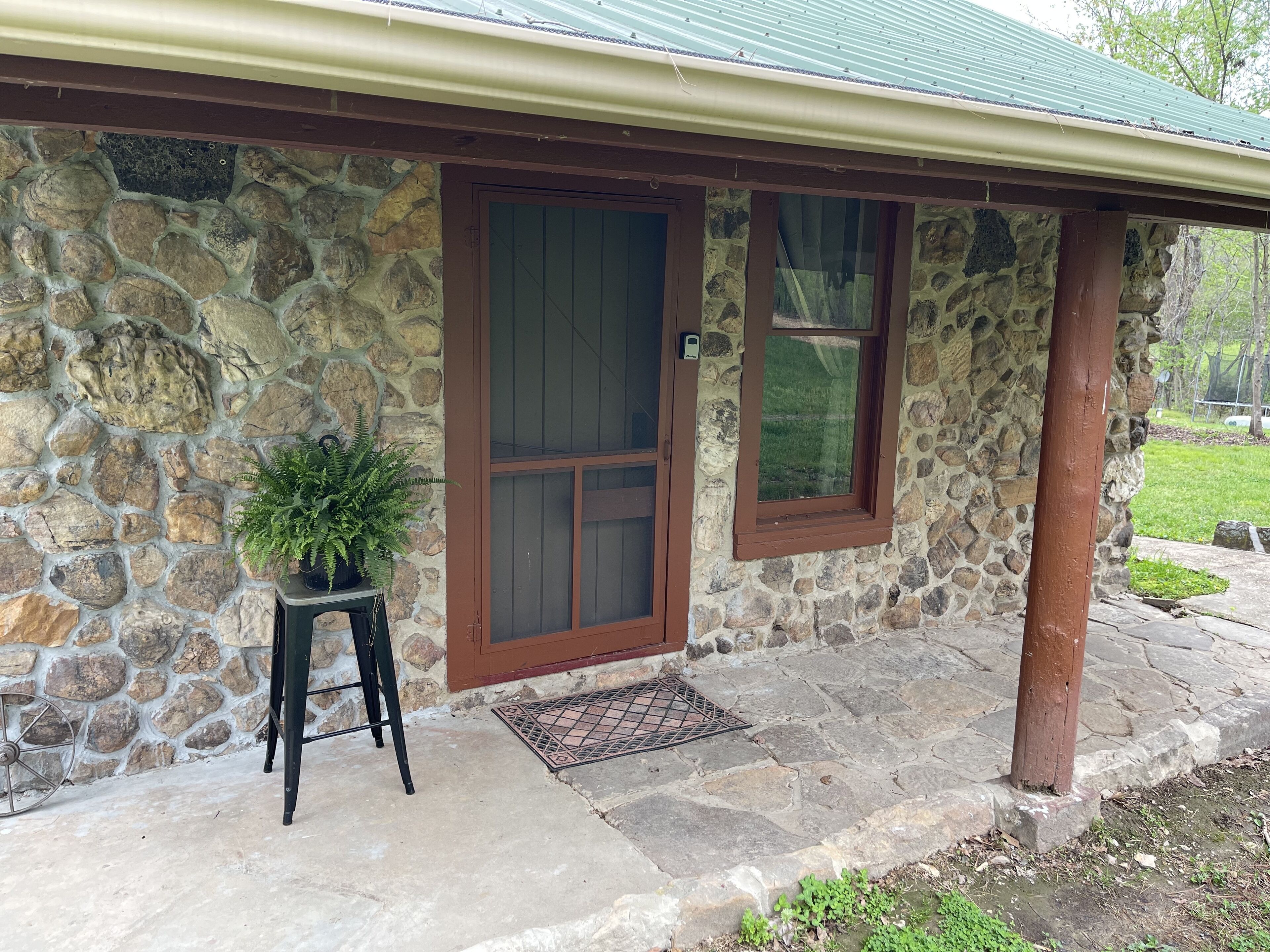 A stone house with a brown door and windows, a small potted plant, and a stone pathway.