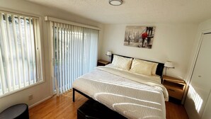 A bedroom with a bed, a nightstand, a lamp, a window with blinds, and a painting on the wall.