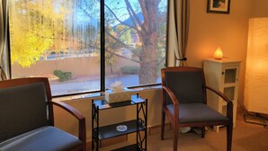 Ein Hotelzimmer mit zwei Sesseln, einem kleinen Tisch, einer Lampe und einem Fenster mit Blick auf Bäume und ein Gebäude.