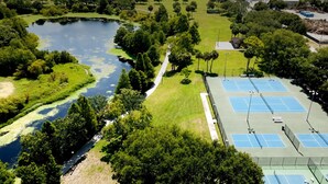 Vista aérea de un parque con cancha de tenis, un estanque y zonas verdes circundantes.