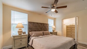 Un dormitorio con cama, mesitas de noche, ventilador de techo y cómoda.