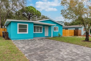 Une maison de plain-pied à l’extérieur bleu, avec une porte d’entrée et un petit jardin devant.