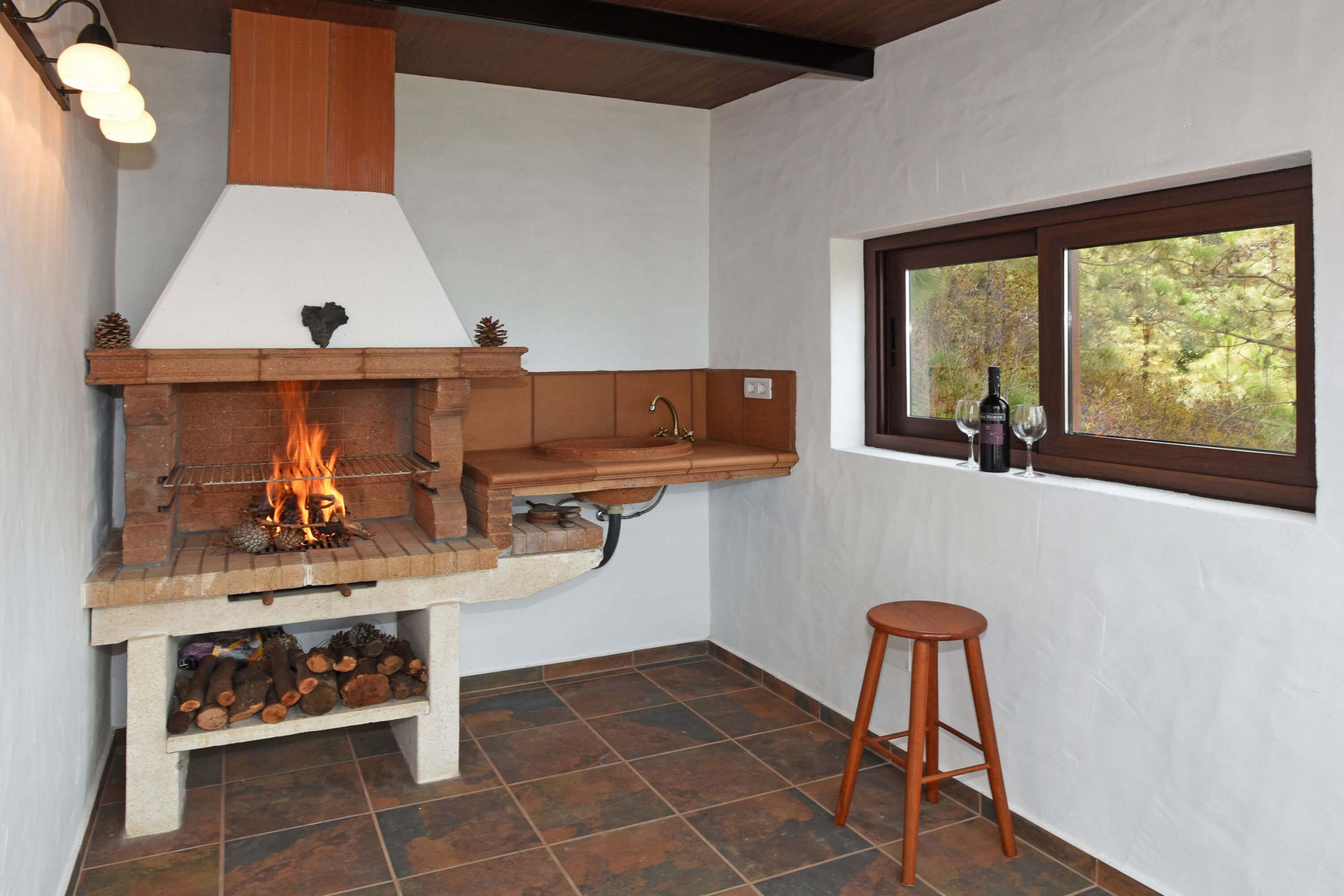 Une cuisine avec un poêle à bois, une fenêtre donnant sur les arbres et un tabouret.