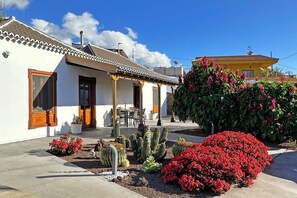 A building with a tiled roof, a patio with outdoor seating, and a garden with cacti and red flowers. - Casa Spica (Los Llanos de Aridane)