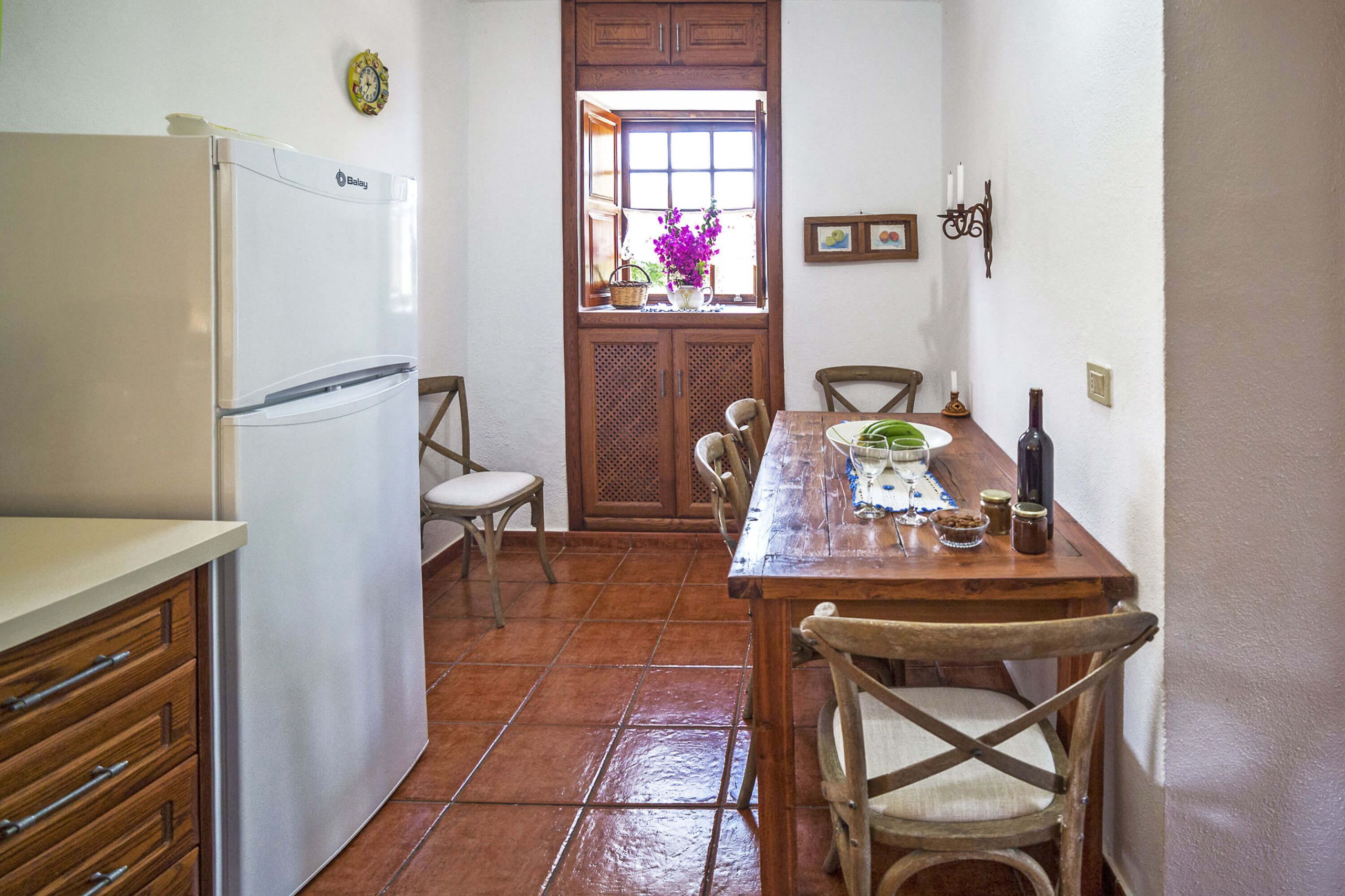 A kitchen with a refrigerator, wooden cabinets, a dining table with chairs, and a window with a view.