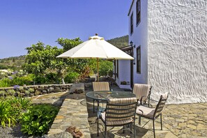 Eine Terrasse im Freien mit einem runden Tisch, gestreiften Stühlen und einem weißen Sonnenschirm.