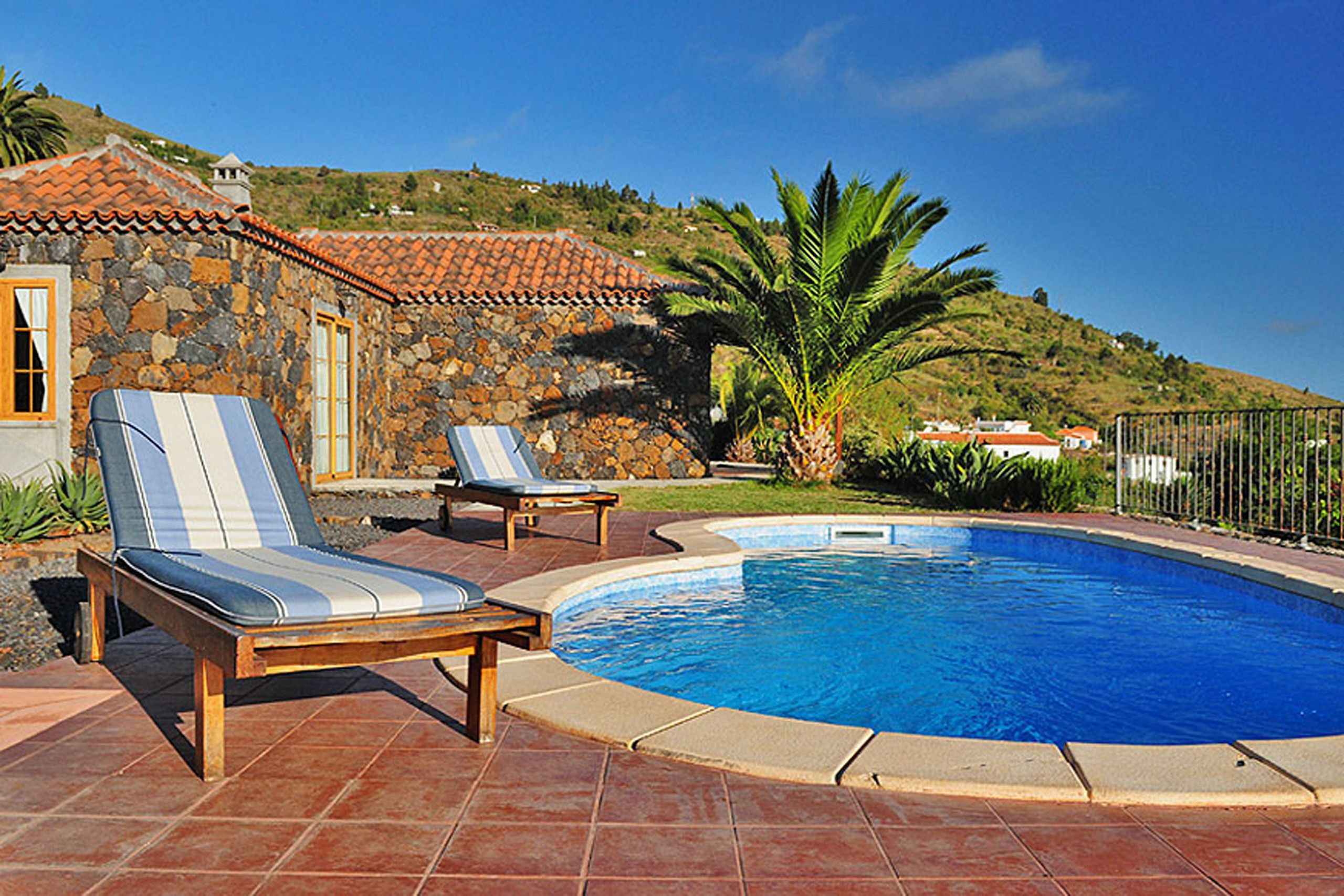 A swimming pool with lounge chairs, a stone building, and a palm tree.