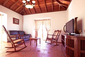 A living room with a wooden ceiling, a television on a wooden cabinet, and a rocking chair.