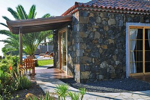 A stone house with a tiled roof, a covered patio, and a pool area.