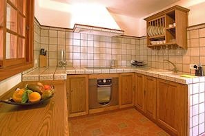 A kitchen with wooden cabinets, a tiled backsplash, a built-in oven, and a fruit bowl on the counter.