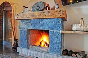 A stone fireplace with a wooden mantel, a brick wall, and a television mounted on the wall.