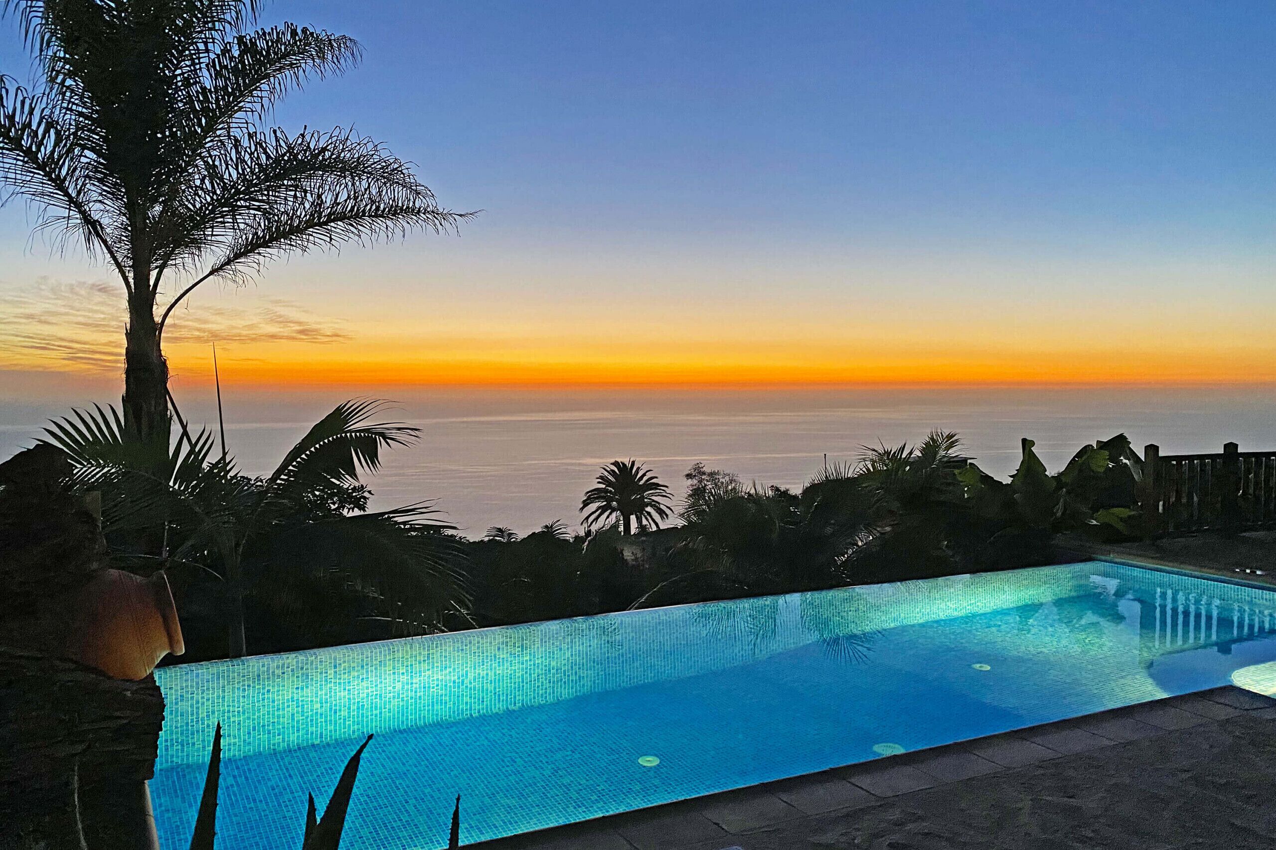 A swimming pool with a view of the ocean at sunset.