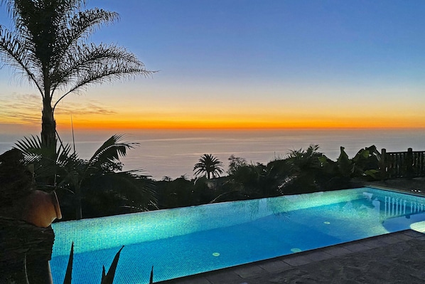 A swimming pool with a view of the ocean at sunset.