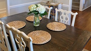 En matplats med ett mörkt träbord, vita stolar, en kristallkrona och en vas med blommor.