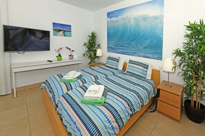 A bedroom with a large bed, a TV, a desk, and a large wave painting on the wall. - Villa Par 4/6 (Maspalomas)