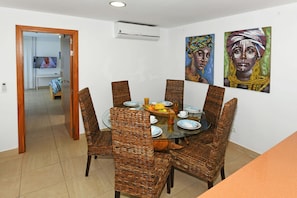 A dining area with wicker chairs, a glass table, and a TV in the background. - Villa Par 4/6 (Maspalomas)