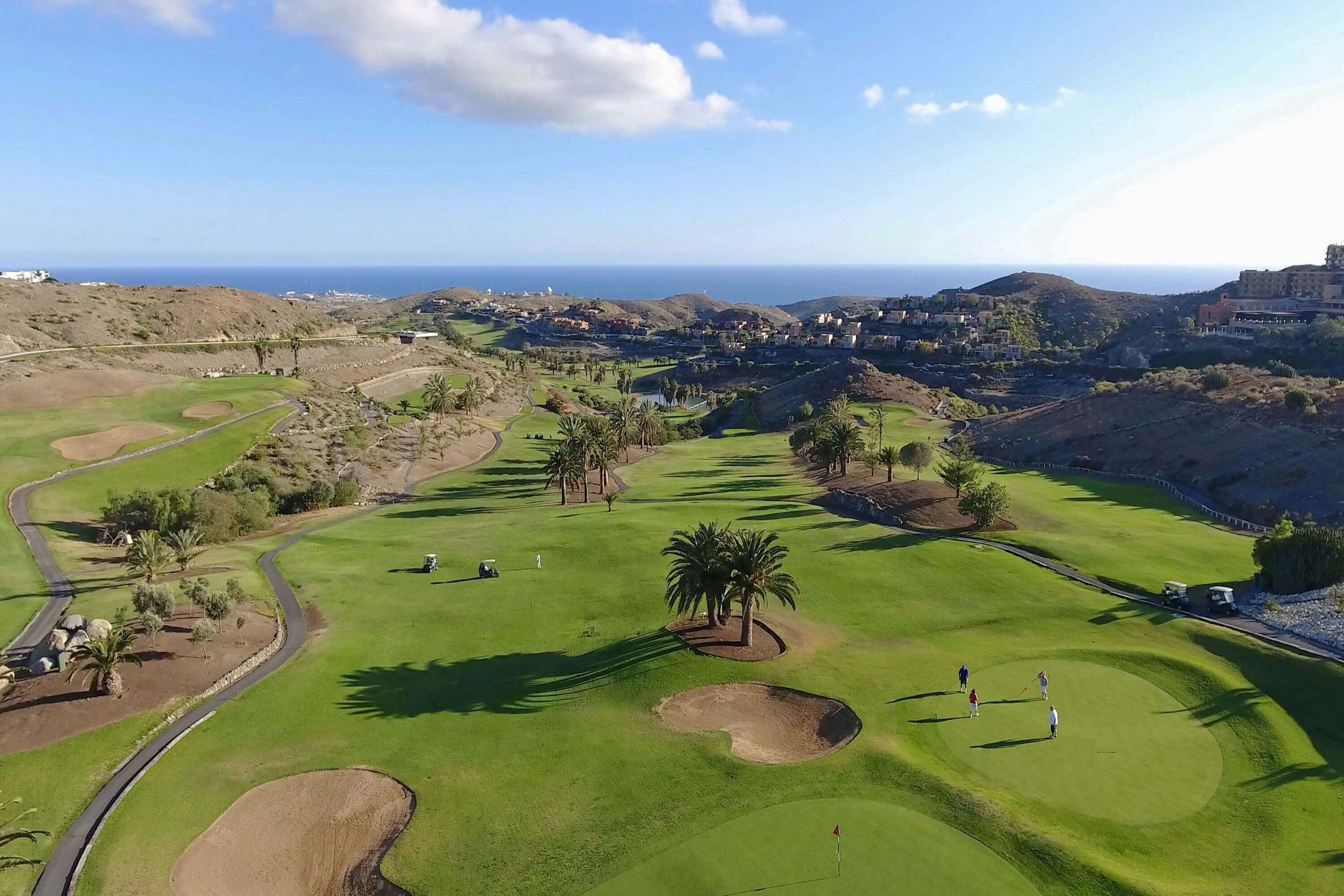 Un parcours de golf offrant une vue sur l’océan et les collines en arrière-plan.