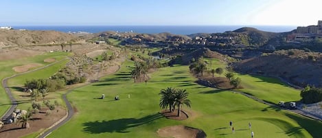 Un campo de golf con vistas al océano y colinas al fondo.