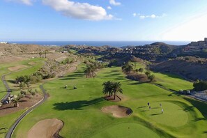 Ein Golfplatz mit Blick auf das Meer und Hügel im Hintergrund.