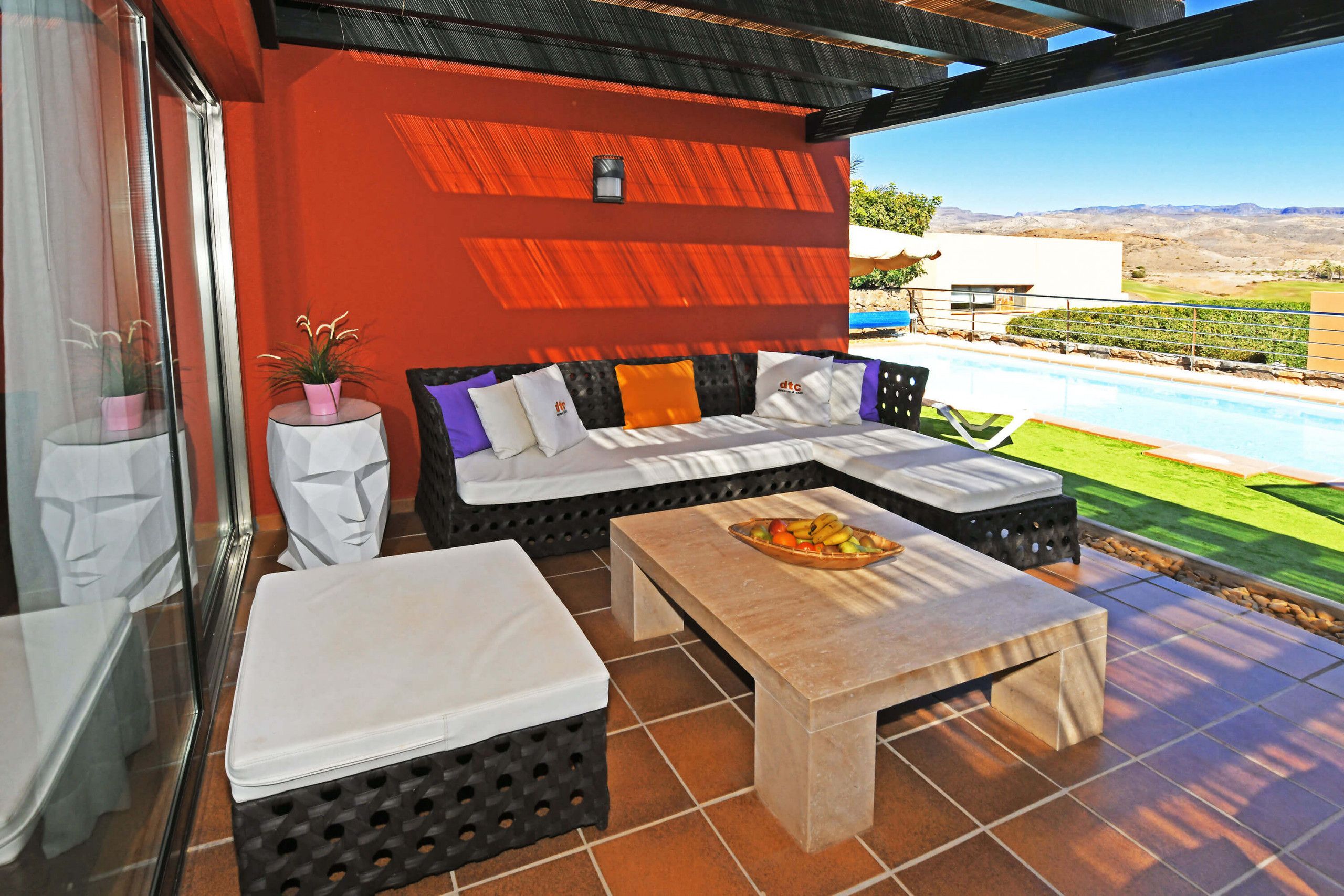 Un espace patio aménagé avec un canapé, une table garnie de fruits et une vue sur une piscine et un paysage.