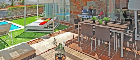 Un patio extérieur moderne doté d’un barbecue, d’un espace salon et d’une piscine.