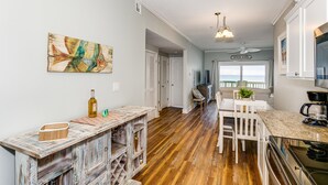 A spacious kitchen with a wooden floor, white cabinetry, and a dining area with a white table and chairs. - Shore Beats Work! Gulf Front! Community Pool! (Penscola Beach)