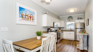 A kitchen with white cabinets, a wooden dining table, and a potted plant. - Shore Beats Work! Gulf Front! Community Pool! (Penscola Beach)