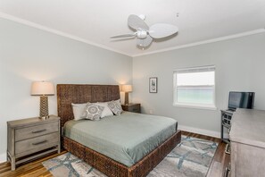Quarto com cama, mesas de cabeceira, ventilador de teto, janela e televisão.