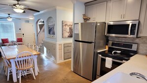 Une cuisine moderne dotée d’appareils électroménagers en acier inoxydable, un coin repas avec des chaises blanches et un escalier menant à un niveau supérieur.