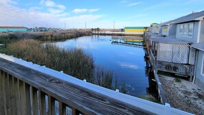 Une propriété située au bord de l’eau, dotée d’une terrasse en bois offrant une vue sur une étendue d’eau calme, et entourée de végétation et de bâtiments au design simple et fonctionnel.