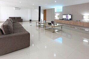 A modern living room with a sectional sofa, a glass coffee table, and a flat-screen TV mounted on the wall.