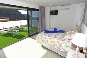 A hotel room with a bed, a TV, a window with a view of a balcony, and a ceiling fan.