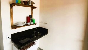 A compact kitchen with a built-in oven, a small refrigerator, and a wall-mounted air conditioner. - Conforto e Sossego: Chalés à Minutos Da Praia (Prado)