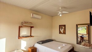 A room with a bed, a desk, a chair, a ceiling fan, an air conditioning unit, and a window with a view. - Conforto e Sossego: Chalés à Minutos Da Praia (Prado)