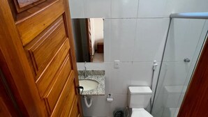 A bathroom with a wooden door, a sink, a toilet, and a shower area. - Conforto e Sossego: Chalés à Minutos Da Praia (Prado)