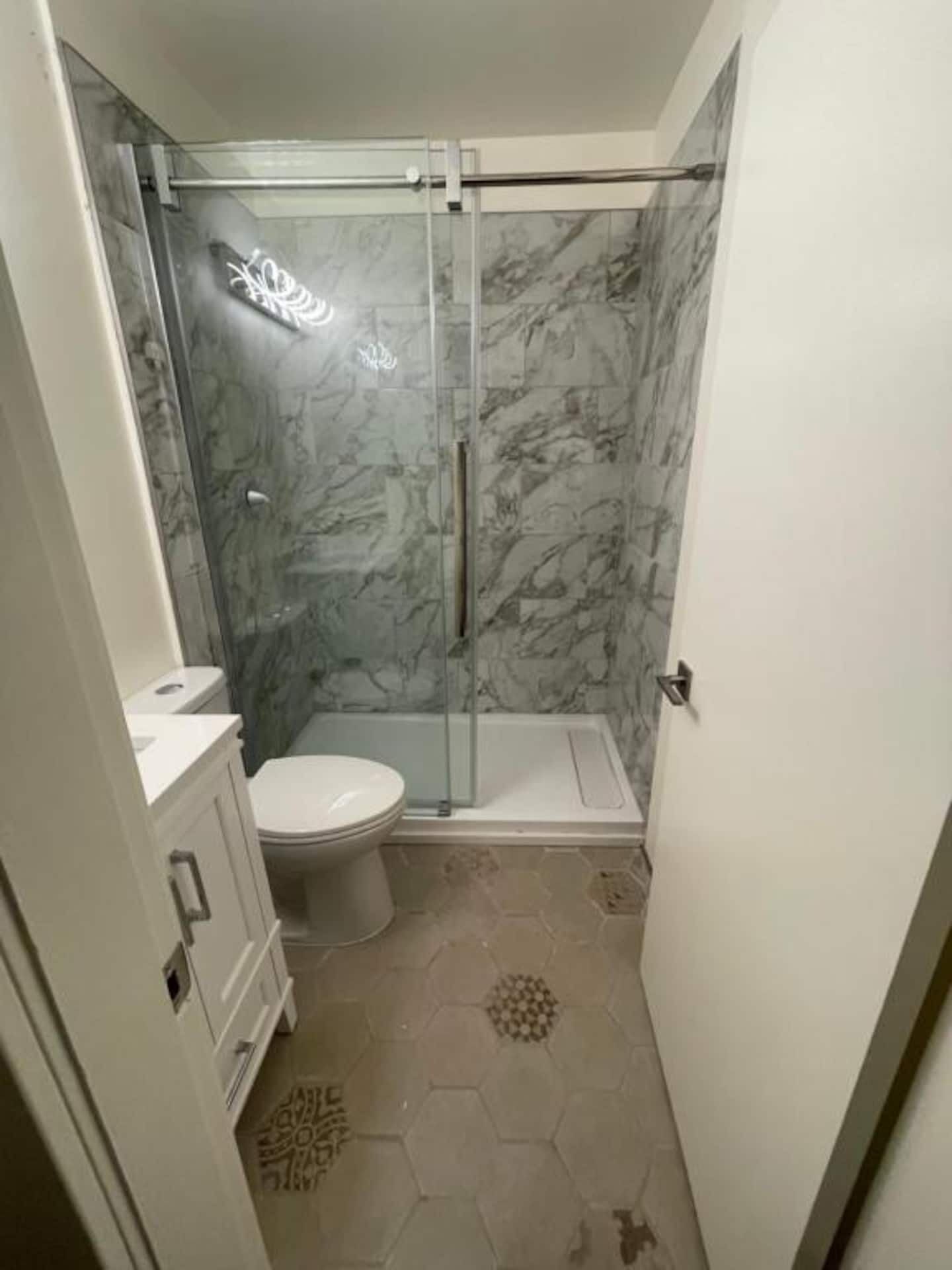 Une salle de bain avec une douche à parois de verre, des toilettes et un meuble-lavabo avec des tiroirs.