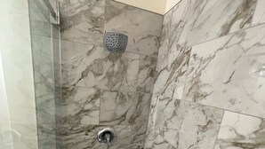 Une douche dotée d’un pommeau de douche à effet pluie et d’un pommeau de douche à main, de murs en marbre et d’une paroi de douche en verre.