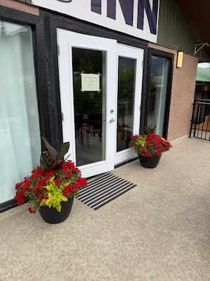 A building entrance with a sign for 'Simple Continental Breakfast,' a door, and two potted plants with red flowers.