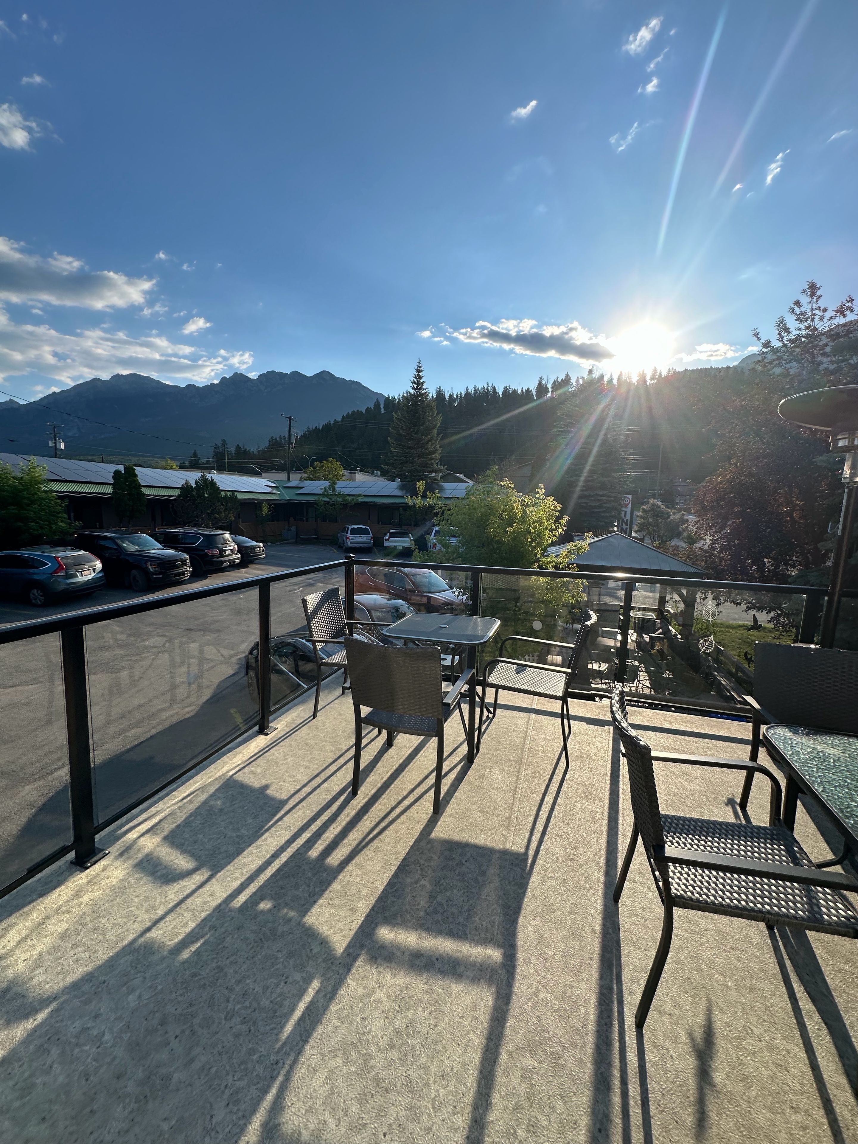 A terrace with outdoor seating, a view of mountains, and parked cars.