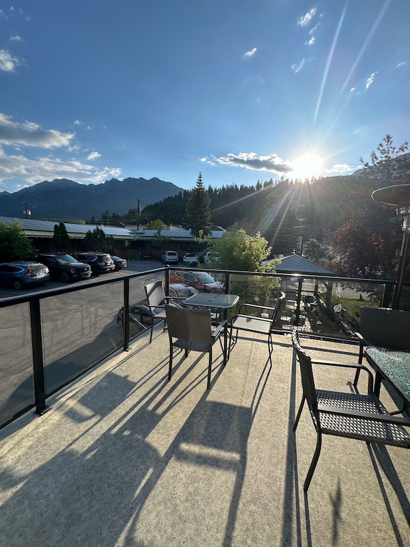 A terrace with outdoor seating, a view of mountains, and parked cars.