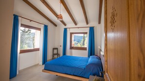 A bedroom with a bed, a wooden wardrobe, and a window with curtains. - Villa Capelvenere (Corbezzolo) (Dorgali)